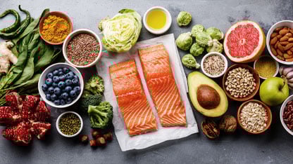 Una variedad de alimentos saludables que incluyen salmón, verduras, frutas, frutos secos, semillas y granos.