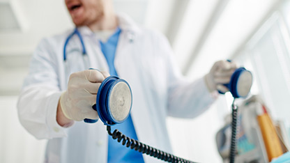 Doctor sosteniendo paletas de desfibrilador, preparándose para administrar una descarga en un entorno de emergencia médica