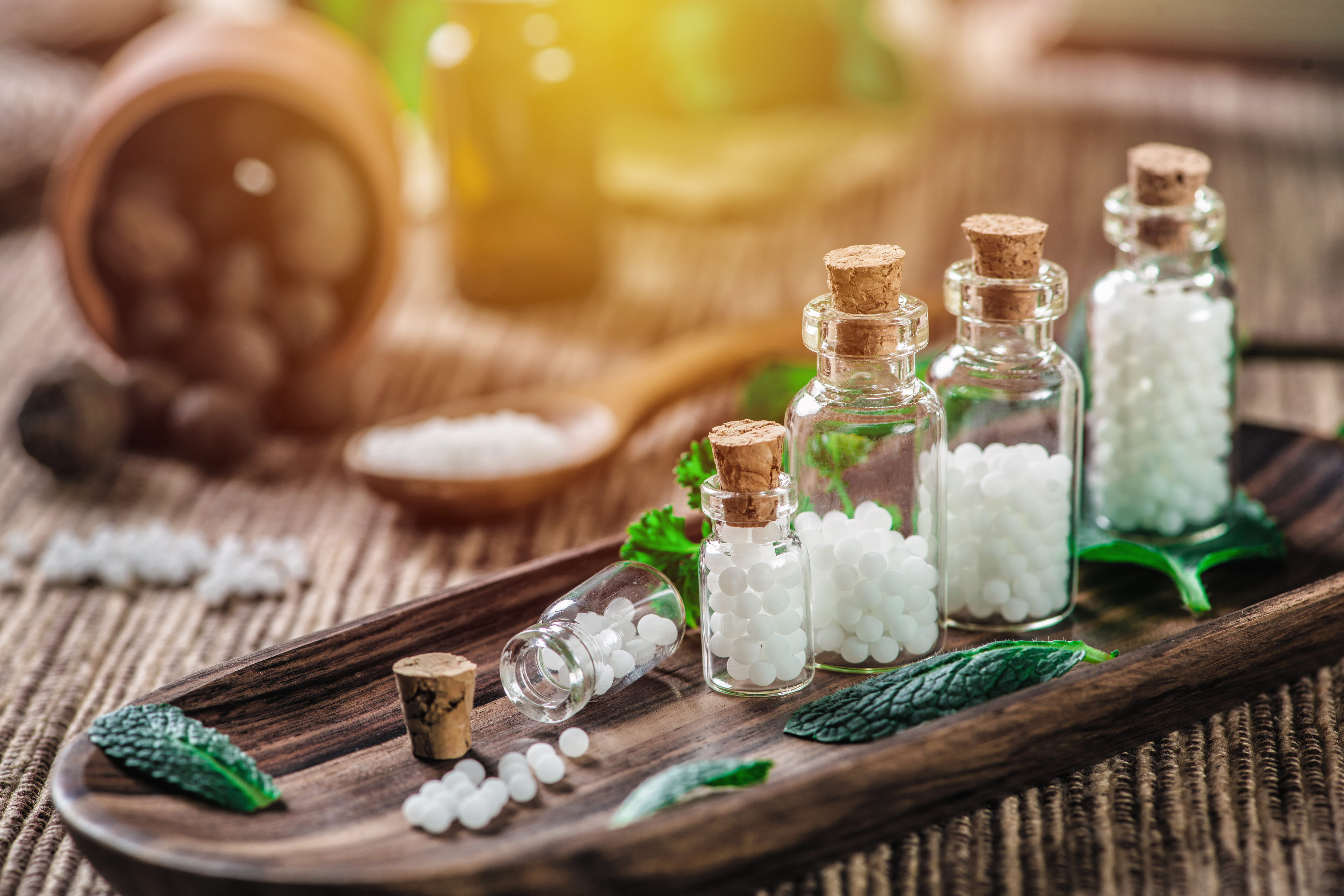 Frascos de vidrio con remedios homeopáticos y hojas de menta sobre una bandeja de madera.